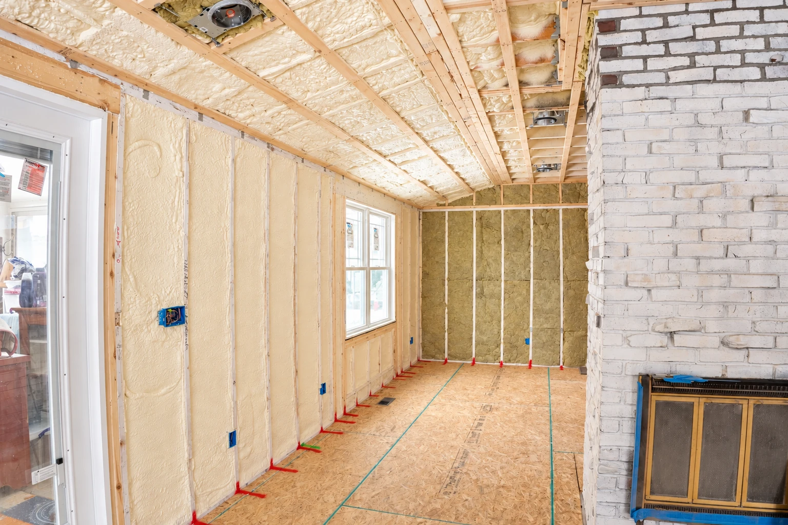 Unfinished room with pale spray foam coating the walls and ceiling, alongside a brick fireplace and exposed framing.