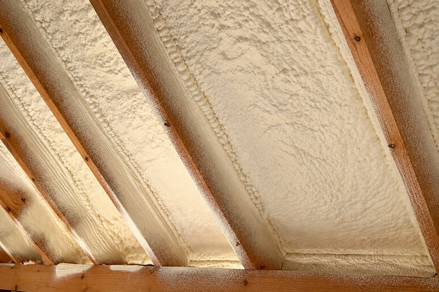 Cream-colored spray foam fills the spaces between exposed wooden rafters.