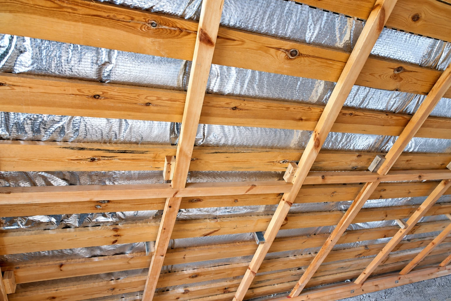 Silver reflective vapor barrier is fitted between wooden roof framing.